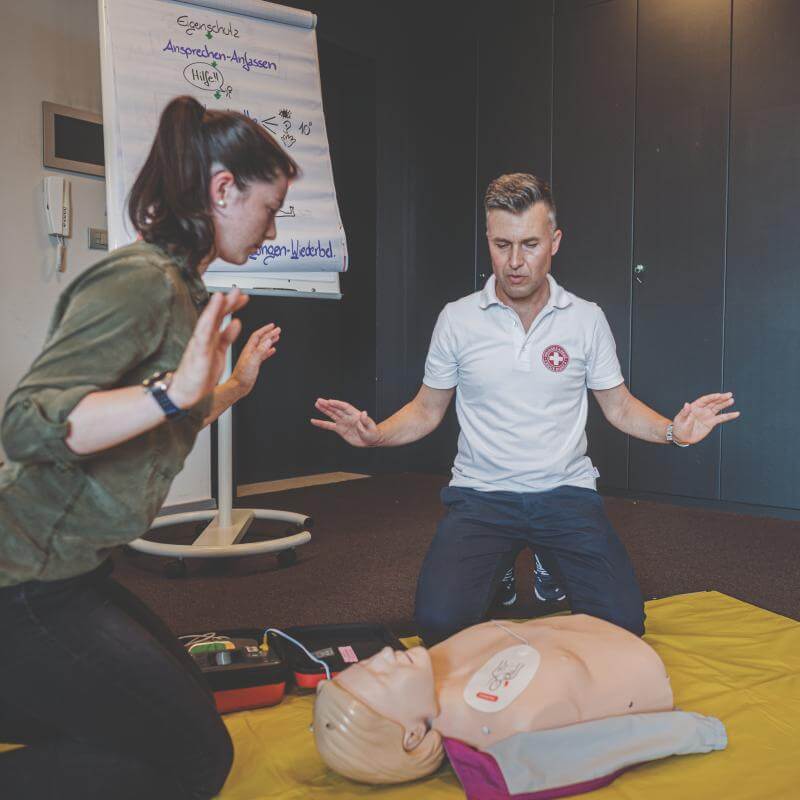 Eine Teilnehmerin bei einem Erste-Hilfe-Kurs des Weißen Kreuzes übt die Herz-Druck-Massage, während ein Instruktor sie instruiert.